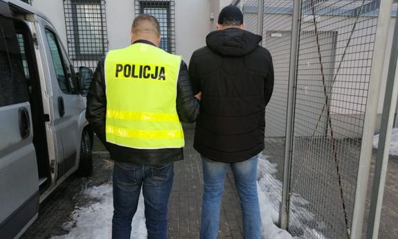 nieumundurowany policjant w żółtej kamizelce prowadzi zatrzymanego mężczyznę