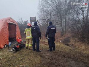 dwaj policjanci funkcjonariusz straży pożarnej stoją przy namiocie ustawionym na skraju lasu