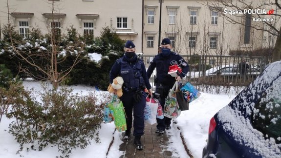 zdjęcie kolorowe: policjantka i policjant niosący prezenty do Domu Dziecka&quot;&gt;