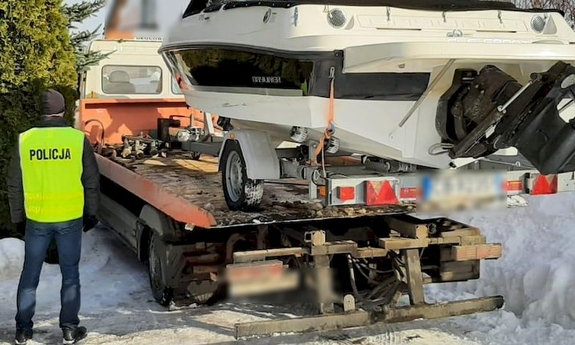 policjant stoi obok lawety, na której znajduje się łódź motorowa