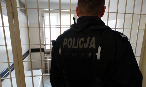 Policjant odwrócony tyłem na tle krat aresztu