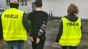 policjanci w żółtych kamizelkach z napisem Policja prowadzą zatrzymanego