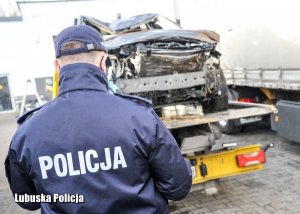 Policjant prowadzi oględziny samochodu znajdującego się na lawecie