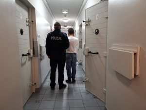 Policjant prowadzi zatrzymanego mężczyznę do celi