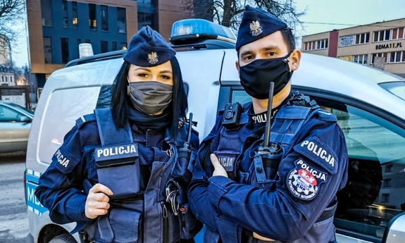 policjant i policjantka stoją przy radiowozie policyjnym