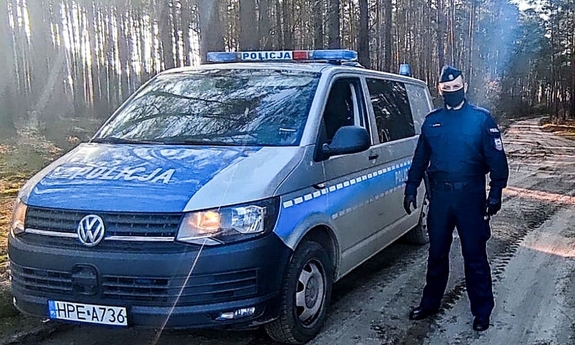 Umundurowany policjant przy radiowozie na drodze leśnej