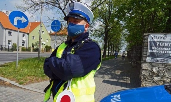 policjant stoi przy radiowozie i patrzy przed siebie