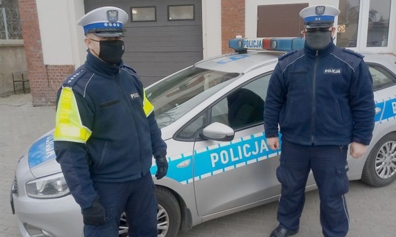 dwaj policjanci stoją przed radiowozem policyjnym
