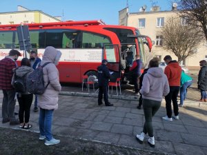 mieszkańcy oraz policjant stoją w kolejce przez autobusem służącym do oddania krwi