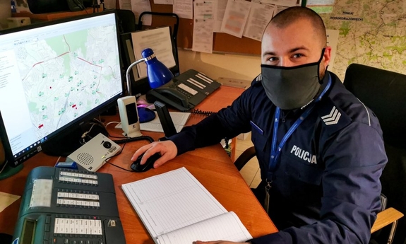 policjant siedzi przy biurku, na którym stoi ekran komputera i klawiatura