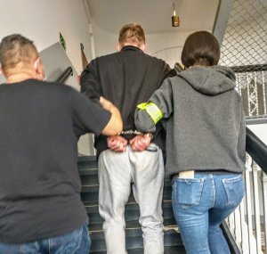 dwoje policjantów prowadzi zatrzymanego mężczyznę po schodach