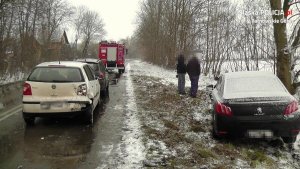 Na zdjęciu widać zaparkowane na drodze samochody osobowe, biorące udział w wypadku, przed którymi stoi wóz strażacki. W przydrożnym rowie znajduje się peugeot.&quot;&gt;
