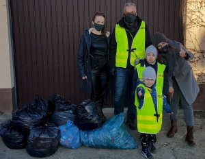 Dwie kobiety, mężczyzna ubrany w żółtą kamizelkę z napisem Policja, dwójka dzieci w żółtych kamizelkach, obok widoczne foliowe worki wypełnione nakrętkami