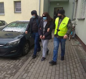 policjant prowadzi zatrzymaną kobietę do radiowozu