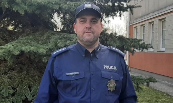 asp. szt. Paweł Kaźmierczak w mundurze. W tle budynek oraz drzewo