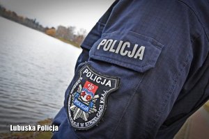 część postaci policjanta i w tle jezioro