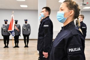 Na pierwszym planie nowo przyjęta policjantka oraz inni policjanci składający ślubowanie. W tle poczet sztandarowy.&quot;&gt;