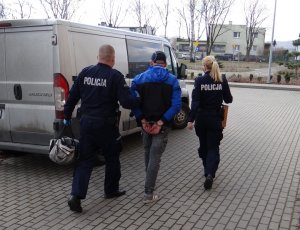 policjant i policjantka prowadzą zatrzymanego do radiowozu