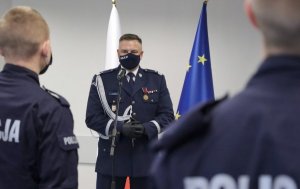 mężczyzna w mundurze stoi przed mikrofonem, z tyłu widoczne są fragmenty flag