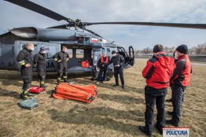 mężczyźni przed policyjnym śmigłowcem, na ziemi leży złożony  zbiornik z wodą, tzw. Bambi Bucket