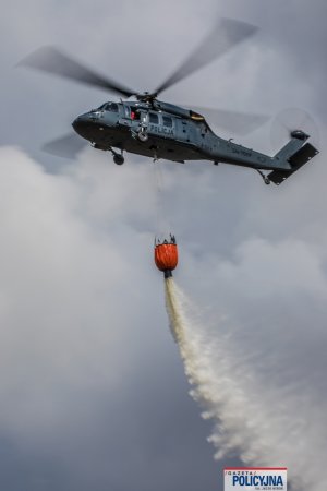 lecący policyjny śmigłowiec z podczepionym zbiornikiem z wodą, tzw. Bambi Bucket