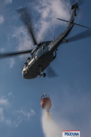 lecący policyjny śmigłowiec z podczepionym zbiornikiem z wodą, tzw. Bambi Bucket