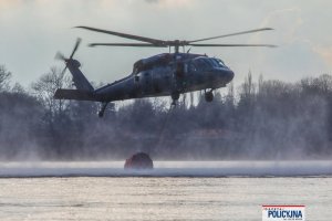 policyjny śmigłowiec podczas lotu nabiera wodę do podczepionego zbiornika