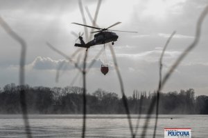 lecący policyjny śmigłowiec z podczepionym zbiornikiem z wodą, tzw. Bambi Bucket