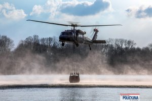 lecący policyjny śmigłowiec z podczepionym zbiornikiem z wodą, tzw. Bambi Bucket