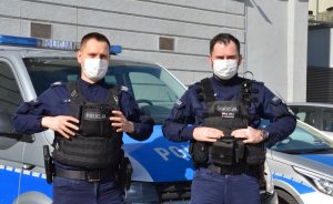 dwaj umundurowani policjanci przy radiowozie