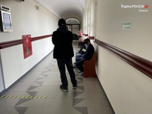 Policjanci pilnują siedzącego na ławce przed sala odpraw zatrzymanego