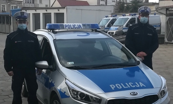 dwaj policjanci stoją obok radiowozu