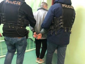 dwaj policjanci ubrani po cywilnemu prowadzą zatrzymanego