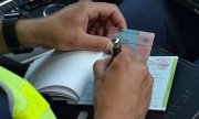 Policjant trzymając w ręku bloczek mandatowy oraz prawo jazdy wypisuje dokumenty