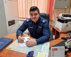 Umundurowany policjant siedzący za biurkiem w pokoju służbowym