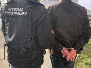 policjant prowadzi zatrzymanego mężczyznę w kajdankach