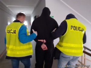 Na zdjęciu widać dwóch policjantów prowadzących zatrzymanego mężczyznę