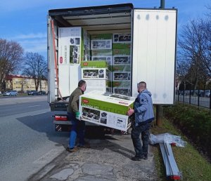 część ładunkowa białego busa, widać pudelka z zestawami mebli ogrodowych, dwóch mężczyzn z maseczkami na twarzy przenosi pudełko z zestawem mebli