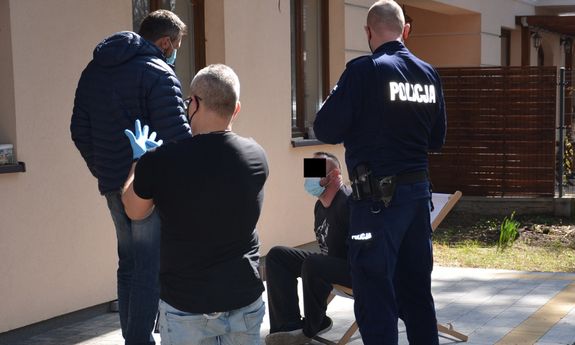 policjant w mundurze i dwaj mężczyźni stoją przy zatrzymanym, który siedzi na leżaku