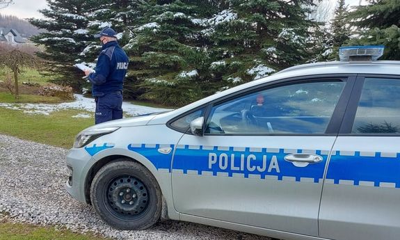 Zdjęcie przedstawia policjanta umundurowanego stojącego obok radiowozu