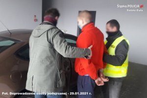 Nieumundurowani policjanci doprowadzają zatrzymanego mężczyznę do pojazdu