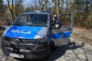 Nowoczesny furgon patrolowy VW T6 stoi w parku, a policjant stoi obok i rozmawia przez radiostację