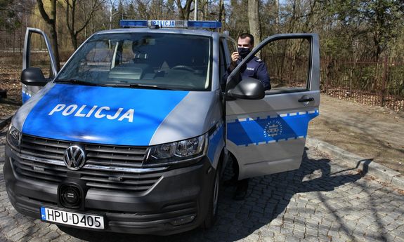 Nowoczesny furgon patrolowy VW T6 stoi w parku, a policjant stoi obok i rozmawia przez radiostację