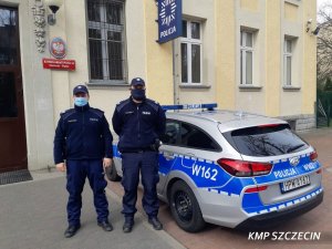 dwóch umundurowanych policjantów na tle komisariatu policji i oznakowanego radiowozu