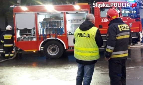 Zdjęcie kolorowe, na którym widać wóz strażacki oraz policjanta i strażaka