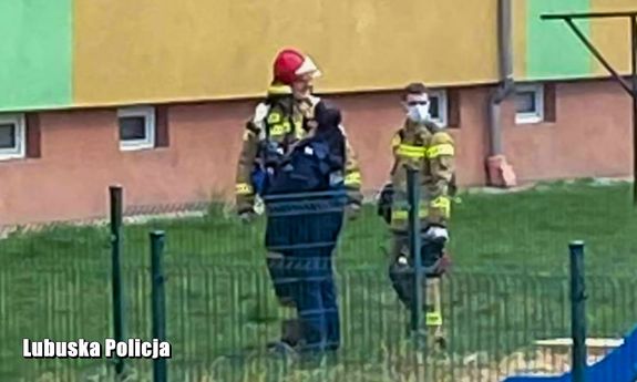 policjantka i strażacy stoją przed blokiem