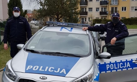 dwaj policjanci stoją przy radiowozie policyjnym z otwartymi drzwiami