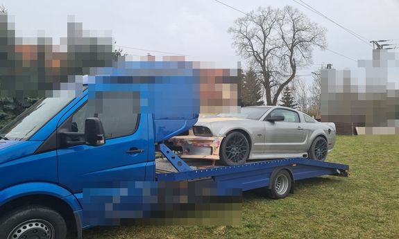 na zdjęciu widać niebieską lawetę a na niej odzyskany samochód, w tle widać drzewa