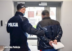 Policjant prowadzi zatrzymanego&quot;&gt;