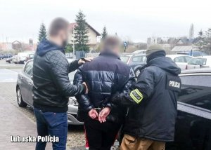 Policjanci kryminalni prowadzą zatrzymanego do radiowozu nieoznakowanego&quot;&gt;